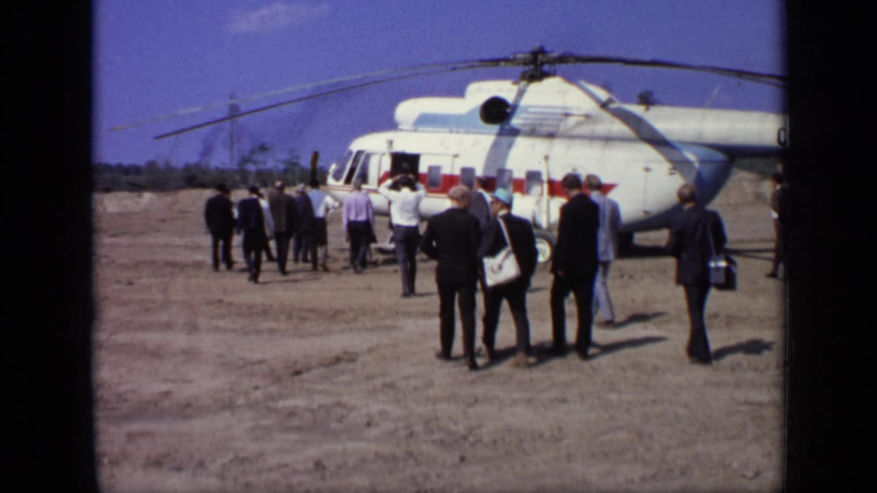 Men in suits and casual shirts continue toward the open door of a Soviet helicopter at a Moscow airfield in 1971.