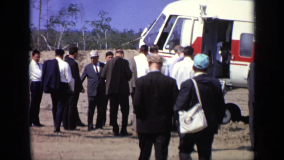 At the Moscow airfield, men gather near the open door and landing gear of the Soviet helicopter, with trees in the background.