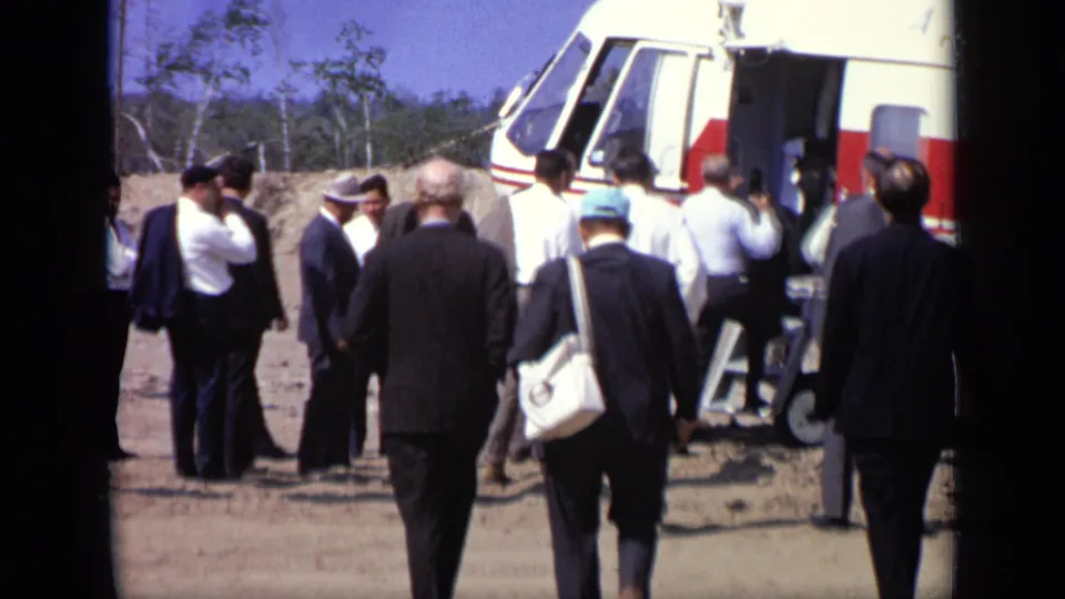 Men in suits and hats stand near the Soviet helicopter entrance in Moscow, with the aircraft nose and open doorway visible.