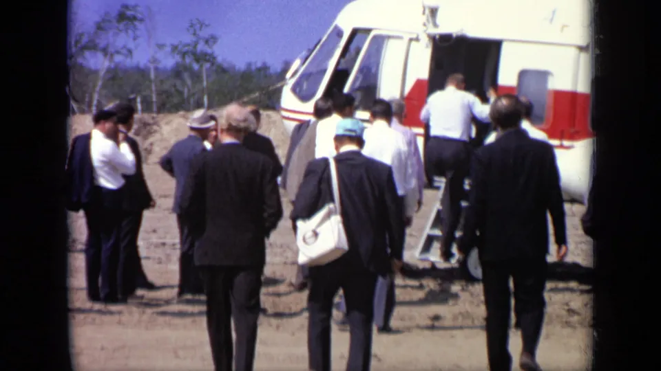 In 1971 Moscow footage, suited adults walk toward steps at a red-and-white helicopter on a sunny dirt airfield.