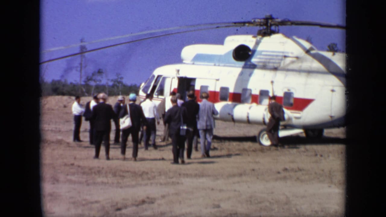 A group stands near a red-and-white helicopter with its side door open.