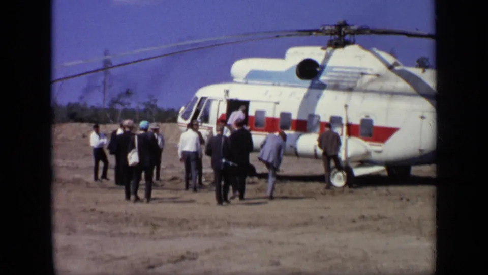 The group remains spread out near the red-and-white helicopter, with some passengers close to the boarding door.