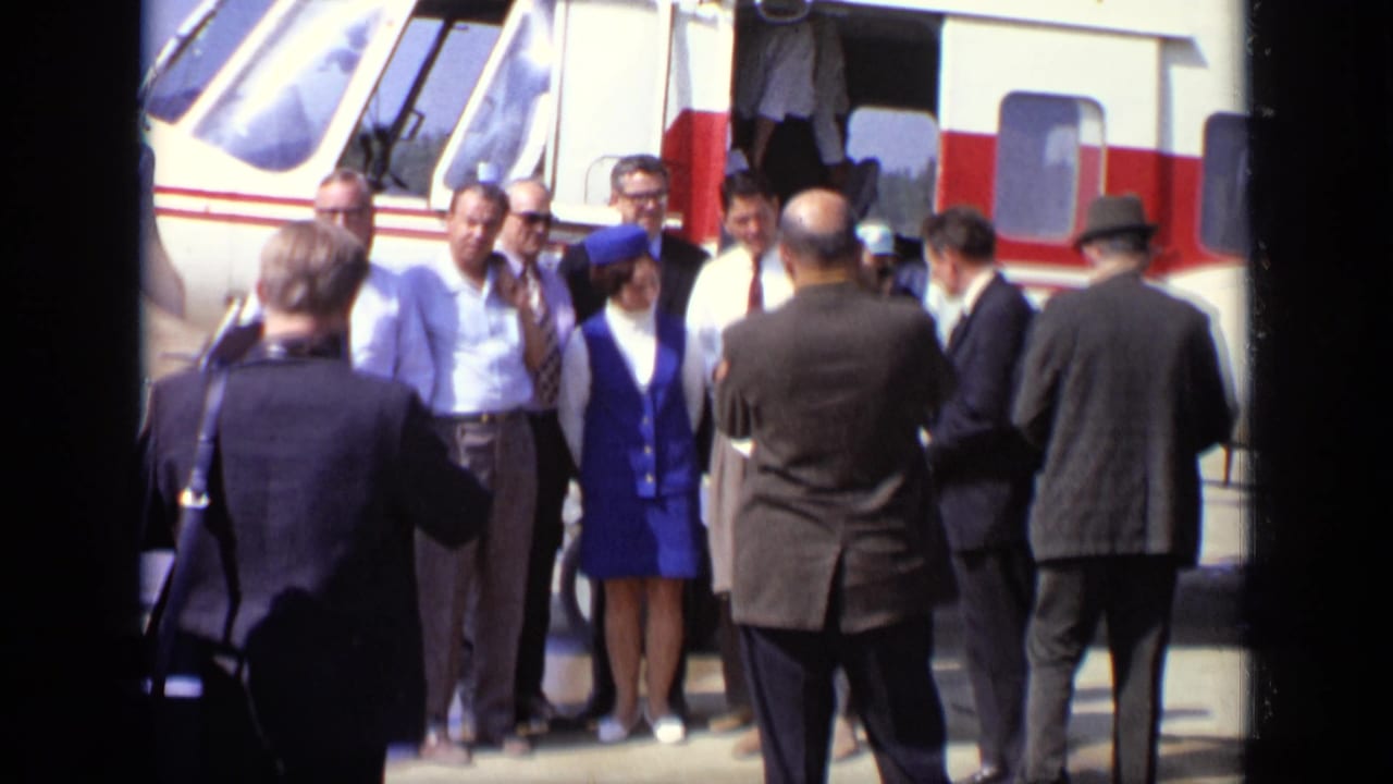 In Moscow, 1971, suited passengers and a woman in a blue flight attendant uniform stand near an open white and red helicopter.