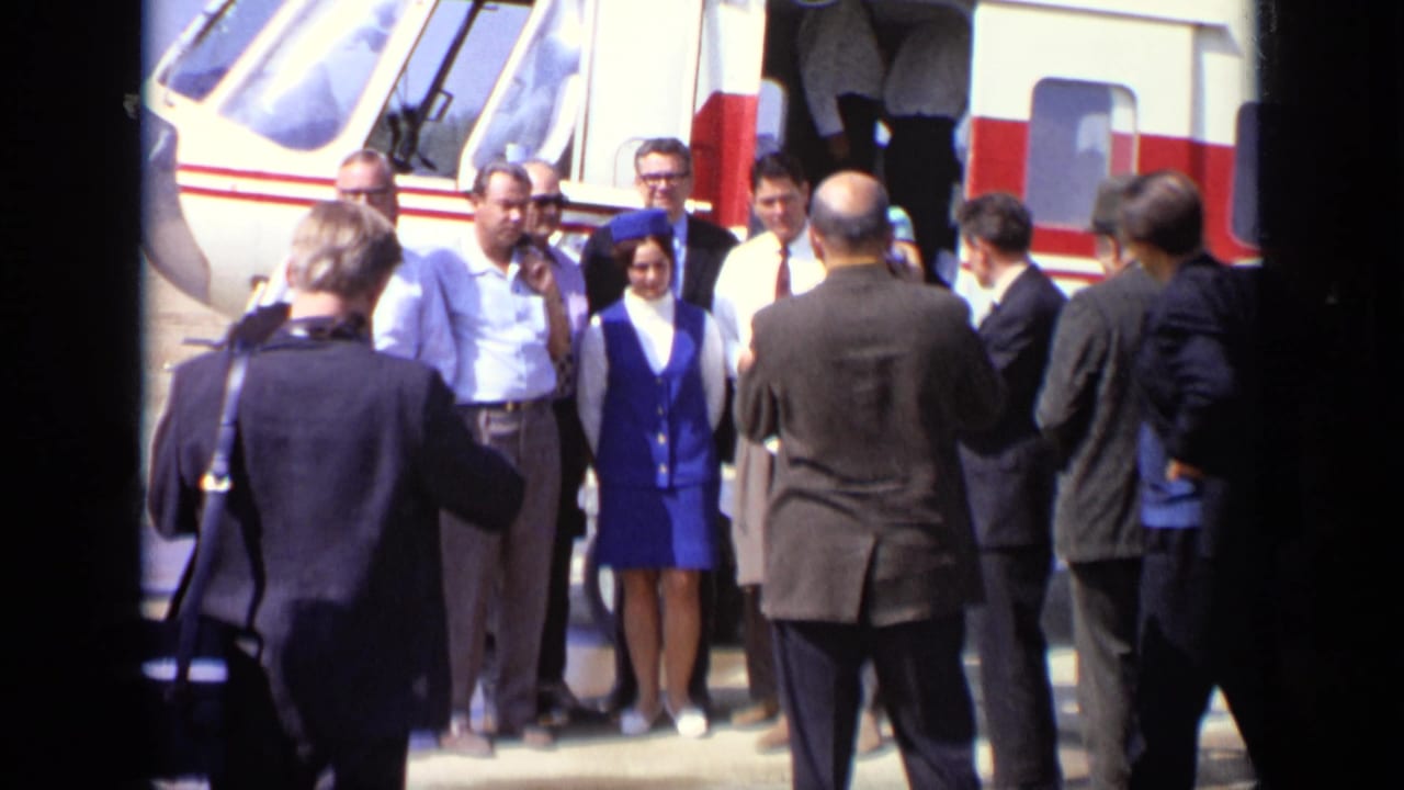 Group posing beside a helicopter with a woman in a blue uniform among suited men.