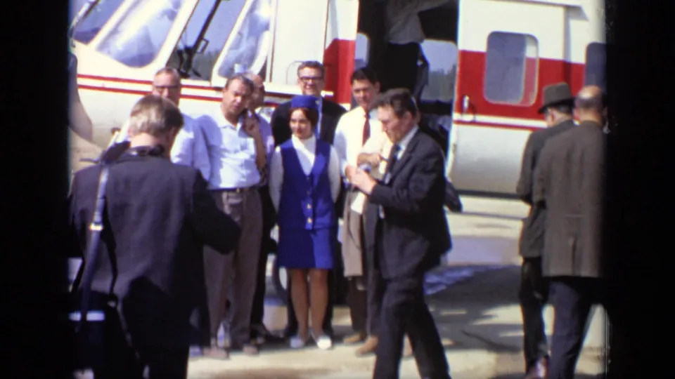 On the Moscow tarmac in 1971, a small passenger group stands near the helicopter as another man crosses in front.