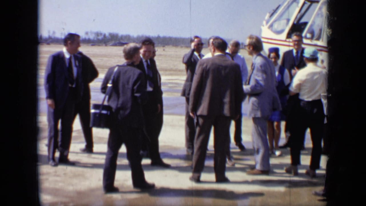 A group of adults talk near the helicopter on the airfield.