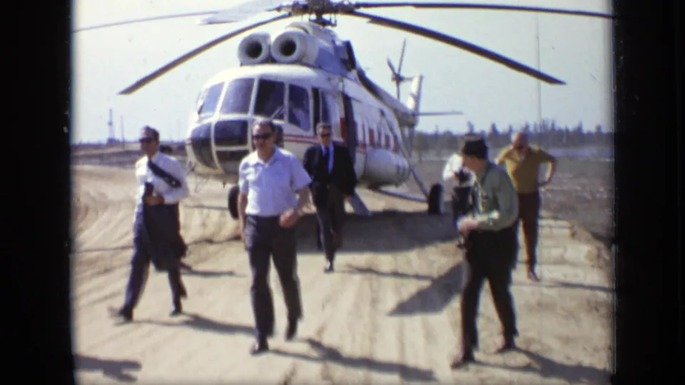 Men, including one holding a camera, walk across a Moscow airfield with the helicopter visible behind them.