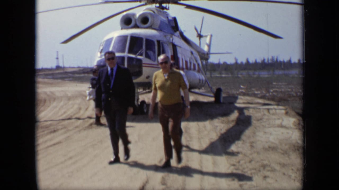 1971 Moscow 8mm frame with a suited man and a casually dressed man walking in front of a parked helicopter.