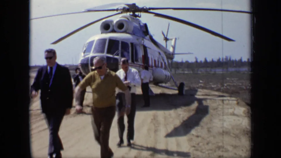 1971 Moscow 8mm frame showing adult men walking past the camera with the helicopter filling the background.