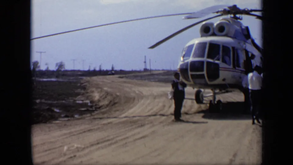 1971 Moscow 8mm frame showing the parked helicopter from farther right, beside a curving dirt road and open airfield.