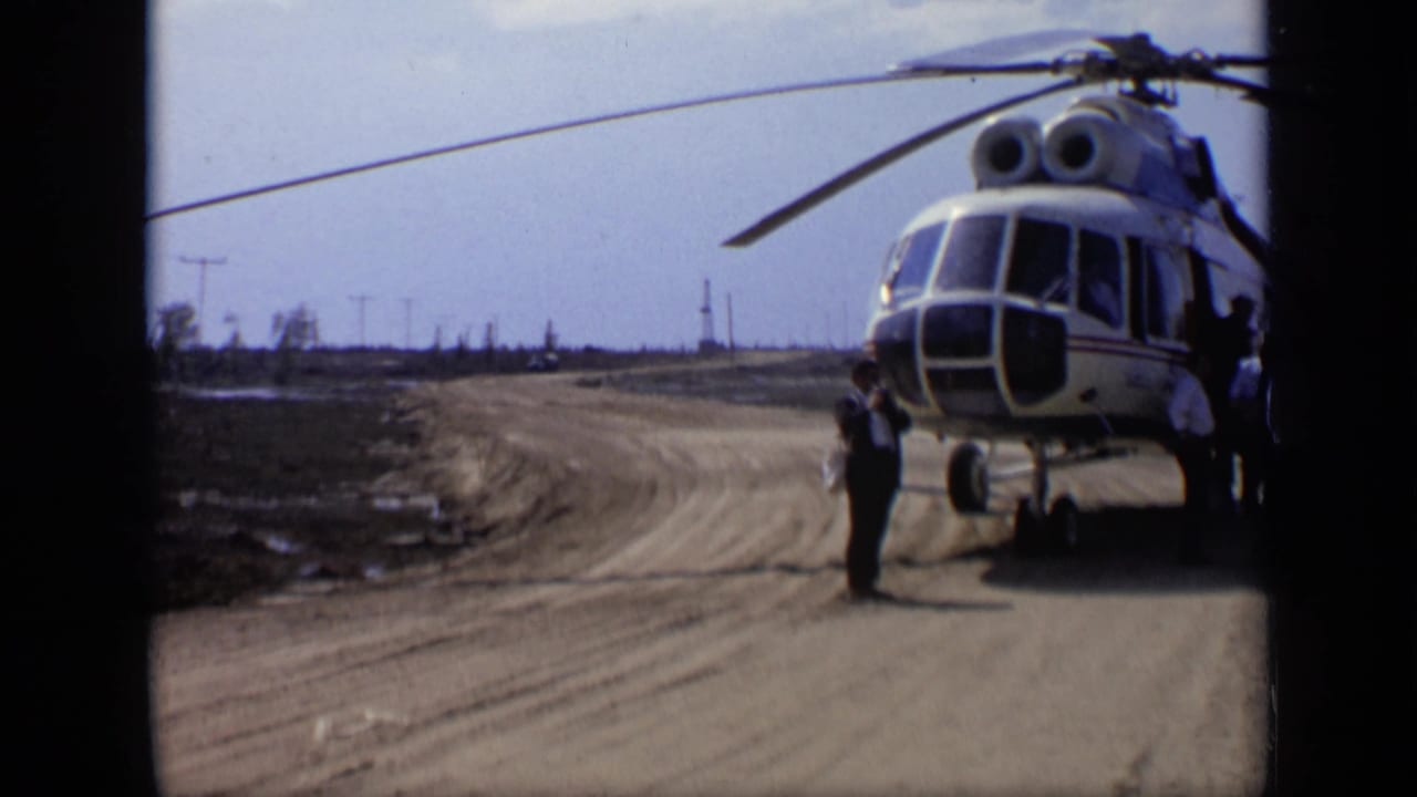 1971 8mm frame from Moscow, Russia metadata showing a helicopter on a dirt road in a sparse, tree-lined field area.