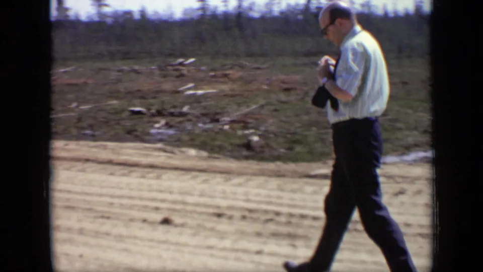 The same adult man moves across the road in the supplied 1971 Moscow, Russia home-movie footage, with sparse trees behind him.