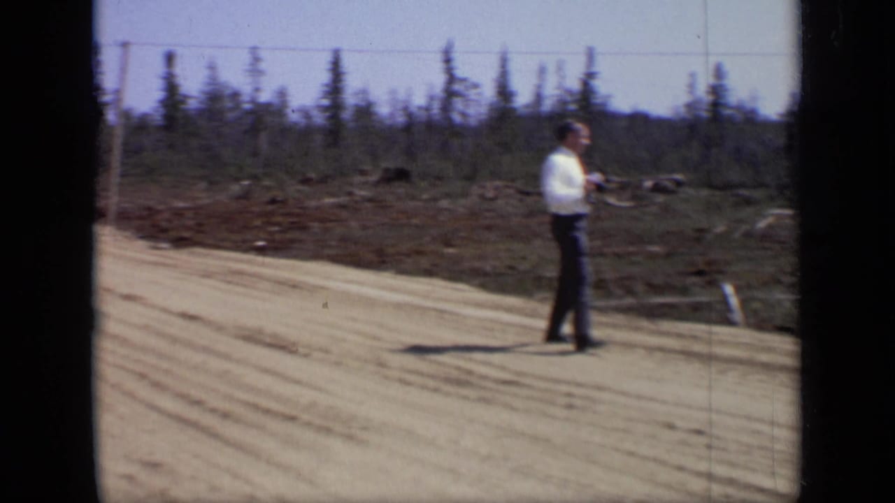 1971 Moscow-area 8mm frame showing an adult man on a sandy dirt road near sparse trees and overhead lines.