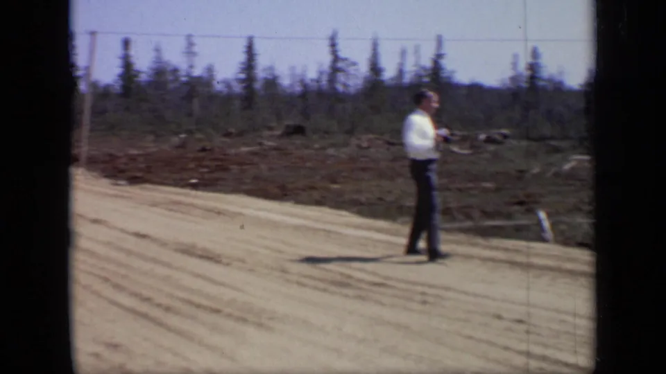 1971 Moscow-area 8mm frame showing an adult man on a sandy dirt road near sparse trees and overhead lines.