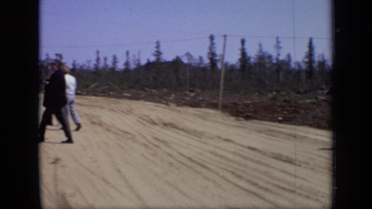 1971 Moscow-area home-movie frame of two adult men crossing a dirt road under a clear sky.