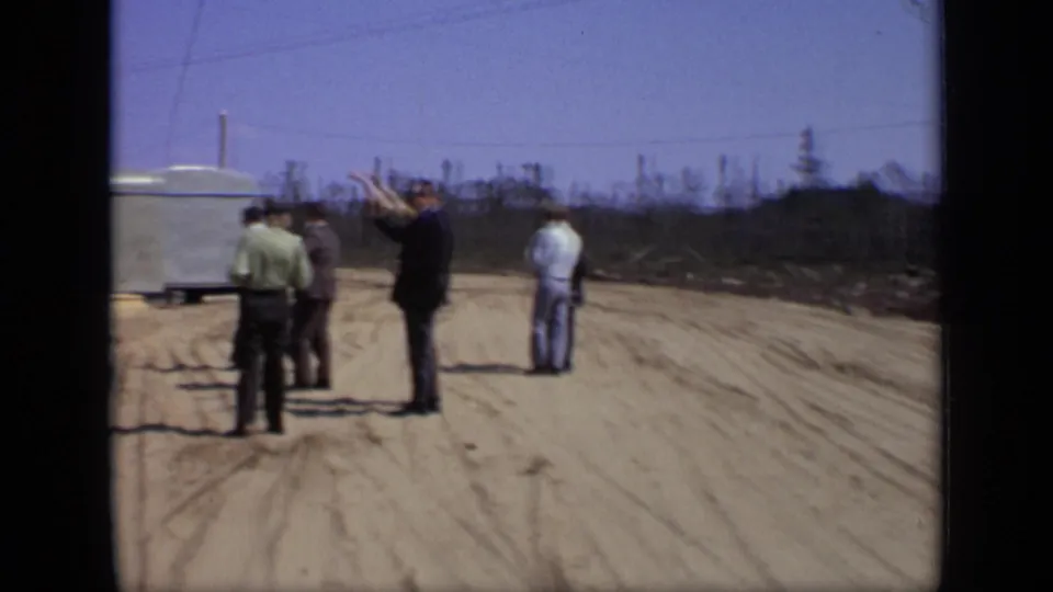 Adult men gather on a rural dirt road near a mobile trailer in 1971 Moscow-area 8mm footage.