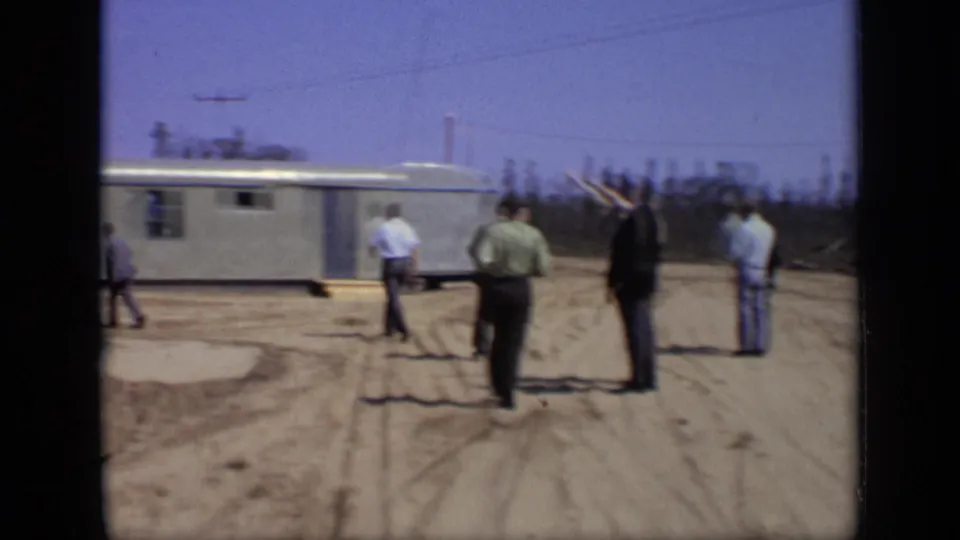 1971 Moscow-area frame showing adult men near a long mobile trailer on a sandy roadside.
