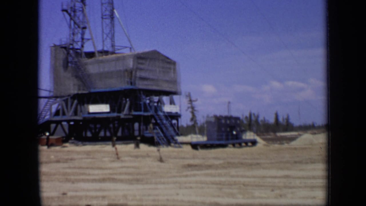 Large raised structure with tower sections, stairs, trailer, and open graded ground.