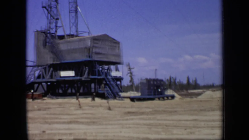 1971 Moscow industrial site with a large elevated structure, metal tower sections, stairs, and a trailer on open ground.
