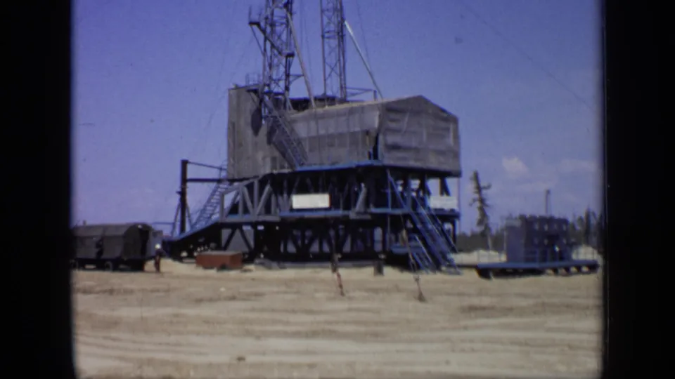 1971 Moscow 8mm frame showing a large raised worksite structure with stairs, tower framework, trailers, and a distant worker.