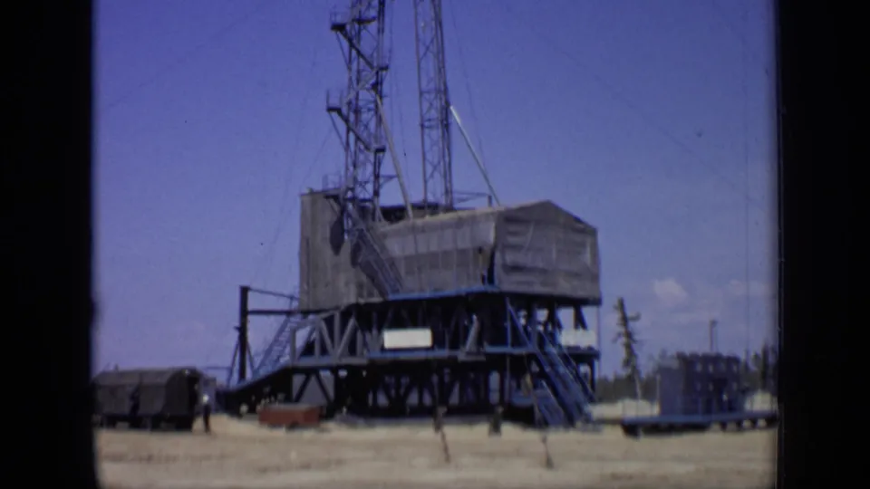 1971 Moscow industrial worksite frame with a towered raised structure, trailers, open ground, and distant trees.