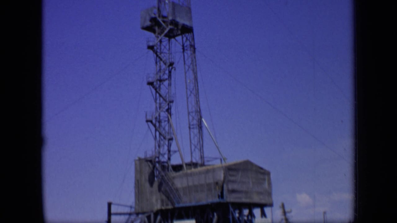 The camera tilt shows the derrick extending above the rig platform, with cables and tower sections visible against the sky.