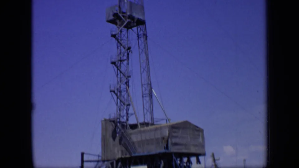 The camera tilt shows the derrick extending above the rig platform, with cables and tower sections visible against the sky.