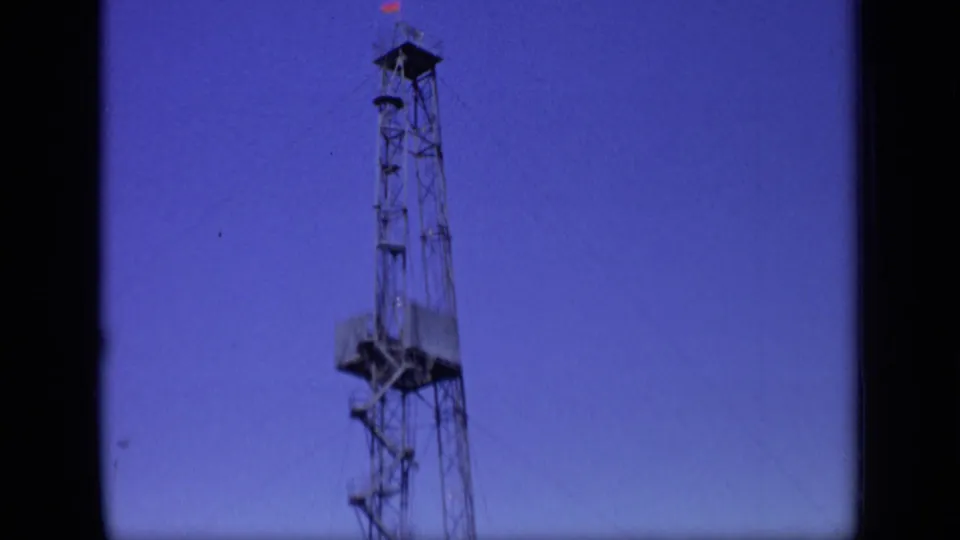 The final frame shows the upper drilling derrick with a small red flag near the top, silhouetted against a clear blue sky.