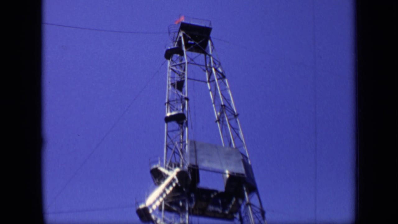 Upper section of a metal drilling rig with platforms and cables against a blue sky.
