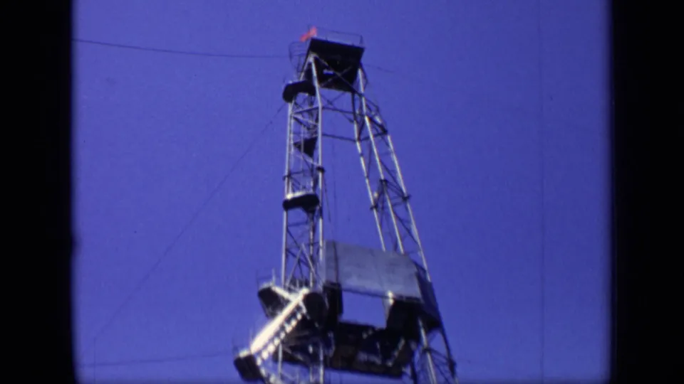 1971 Moscow 8mm frame focused on the upper drilling rig structure, showing platforms, angled supports, and cables against blue sky.