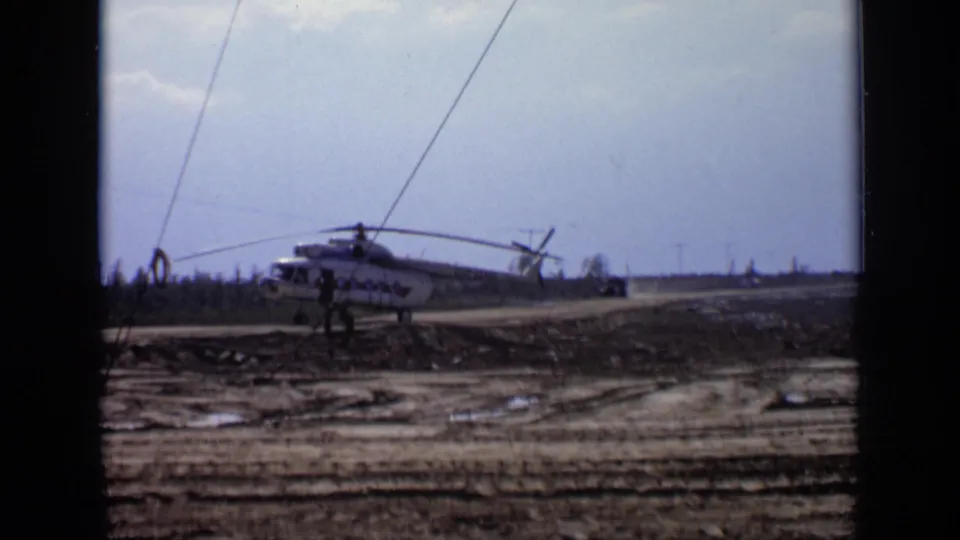 1971 Moscow-area 8mm frame showing a white helicopter with red markings on a muddy forest road as a person stands nearby.