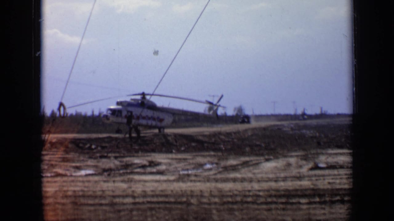 White helicopter on a dirt road with a person nearby and dust farther down the road.