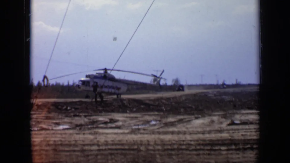 White helicopter with red markings remains on the muddy road near Moscow as a distant vehicle or aircraft raises dust behind it.