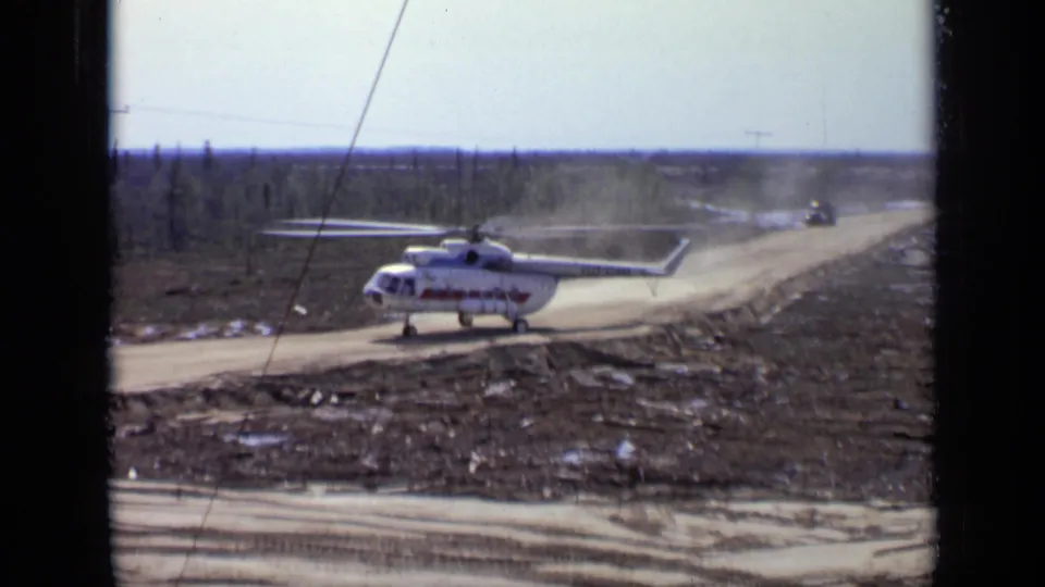 1971 Moscow-area 8mm frame of a white helicopter with red markings moving on a muddy road through sparse forest.