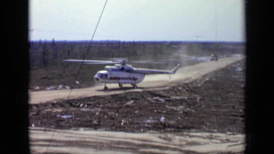 White helicopter with red markings continues along a rough road in the Moscow-area 1971 footage, with dust hanging over the track.