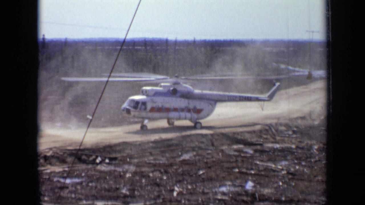 White helicopter with spinning rotor kicking dust from a dirt road.