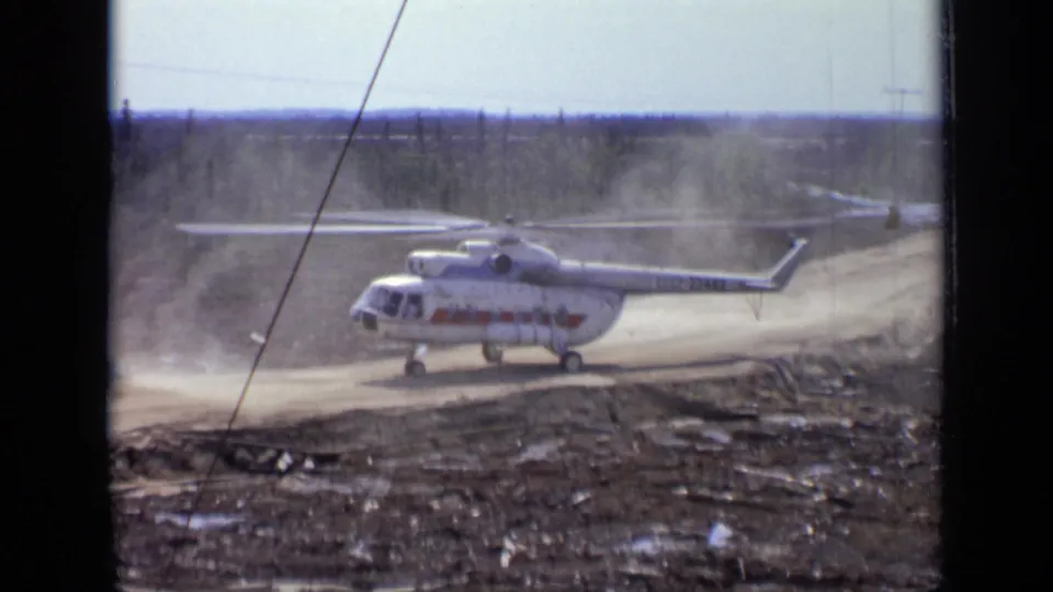 1971 Moscow-area frame of a large helicopter on an unpaved road, its rotor wash lifting dust across the forest edge.