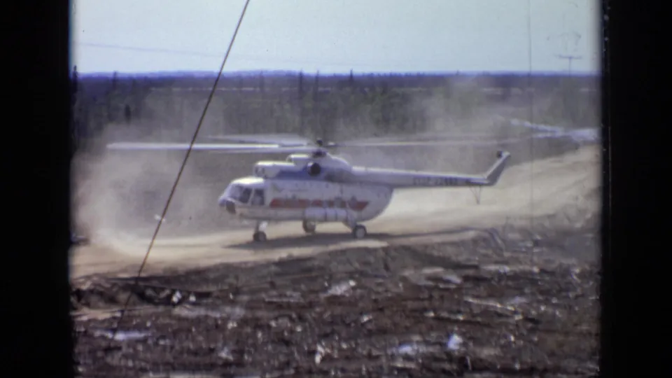 Final 1971 Moscow-area frame showing the white helicopter with red markings amid dust, road curves, and distant trees.