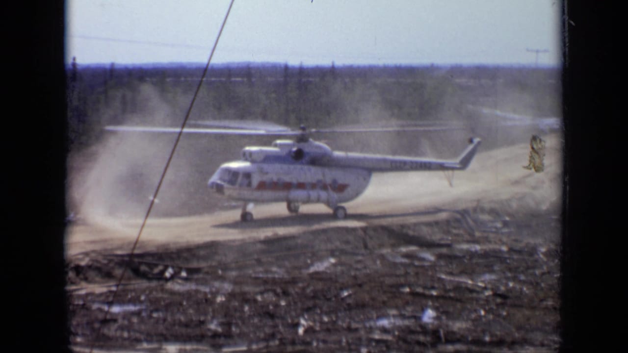 White helicopter on dusty ground with rotor wash beginning to rise.