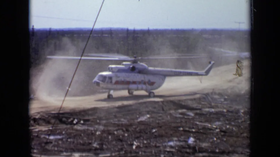 1971 Moscow-area 8mm frame showing a white helicopter with red markings on a dusty unpaved landing zone.