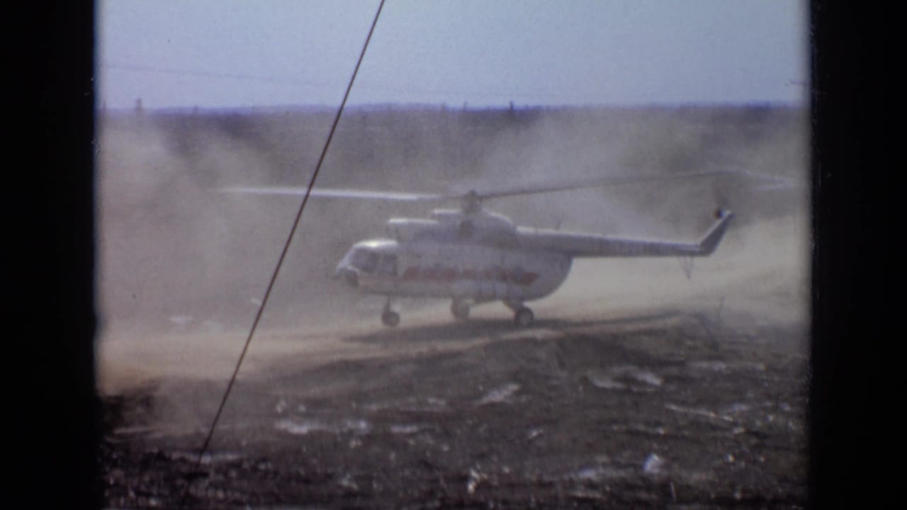 1971 Moscow-area home-movie frame of a helicopter lifting slowly while dust drifts across the landing zone.