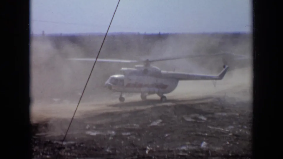 1971 Moscow-area home-movie frame of a helicopter lifting slowly while dust drifts across the landing zone.