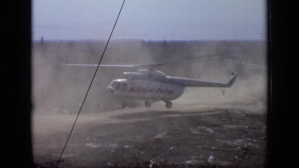 1971 Moscow-area 8mm frame showing the helicopter hovering low as rotor wash pushes dust across the view.