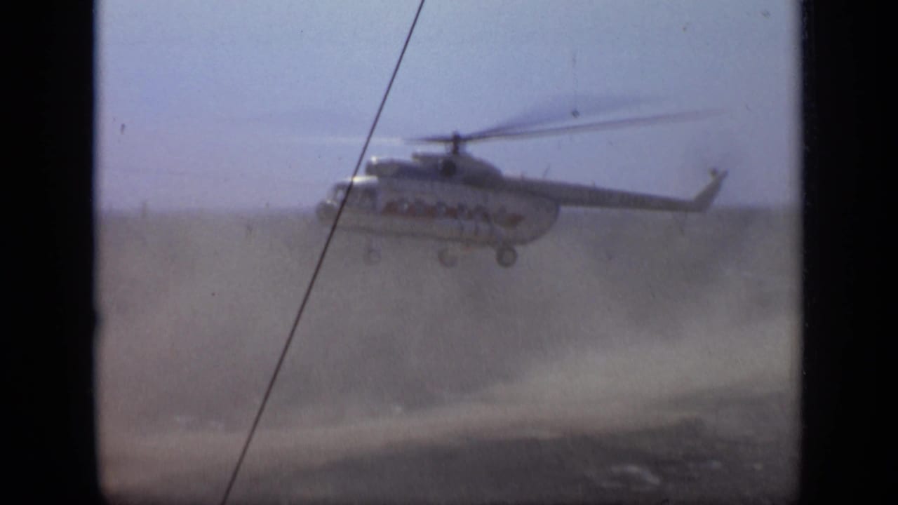 1971 Moscow 8mm frame with a helicopter ascending through dust over an open field, partially framed by film borders and a diagonal line.