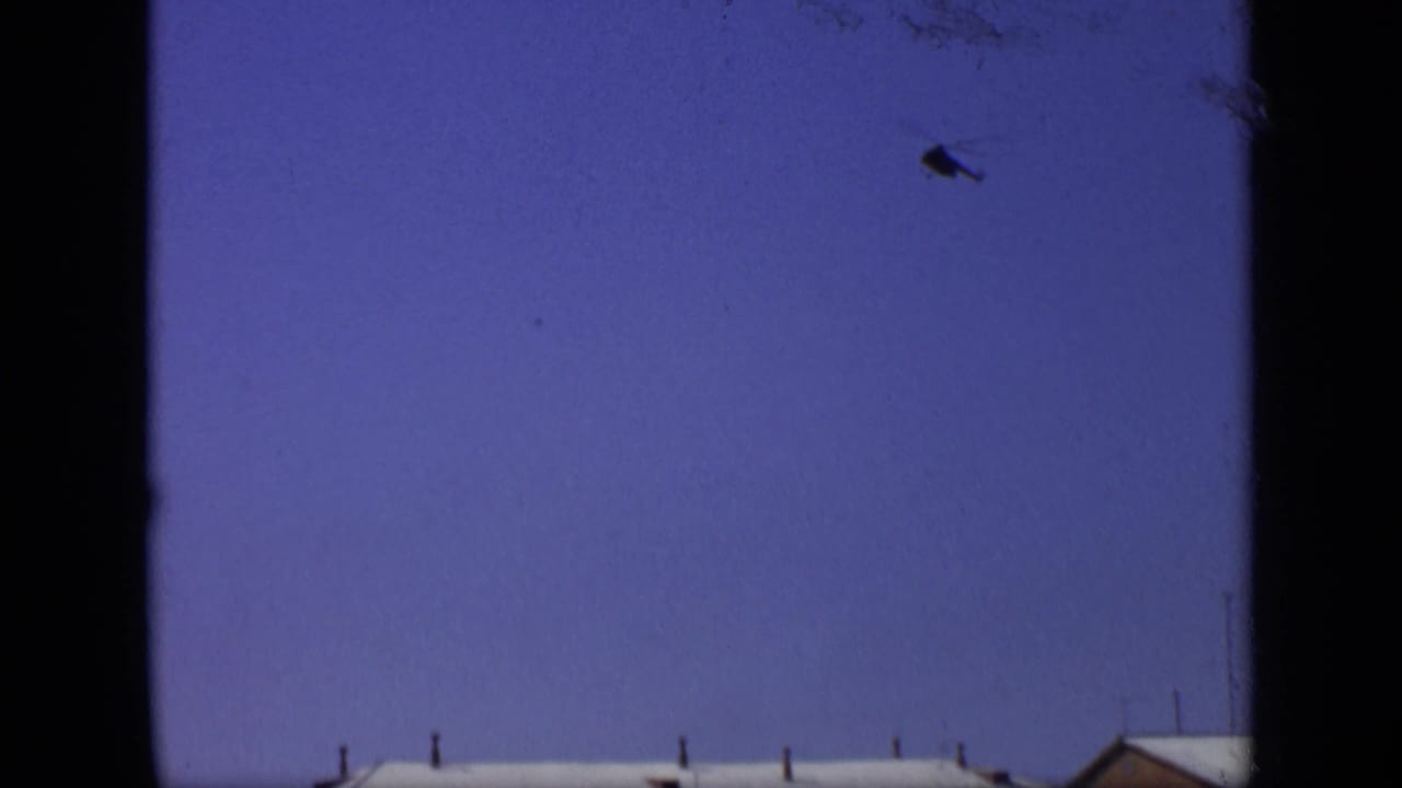 1971 Moscow 8mm frame with blue sky, dark window-like borders, a partial roofline, and a small aircraft shape overhead.