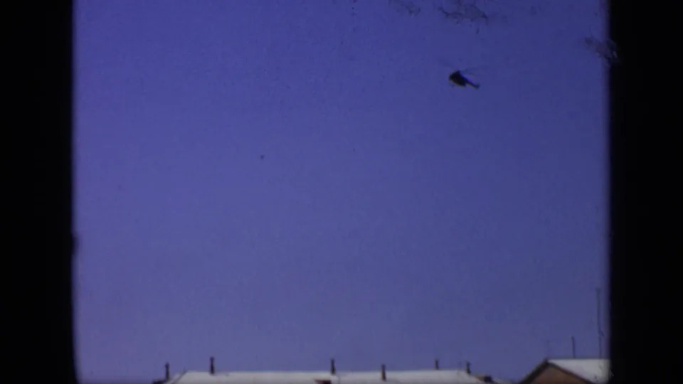 1971 Moscow 8mm frame with blue sky, dark window-like borders, a partial roofline, and a small aircraft shape overhead.