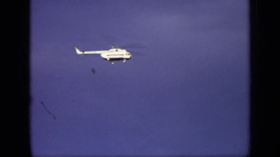 1971 Moscow 8mm frame of a white helicopter in flight against blue sky, with rotor blur and landing gear visible.