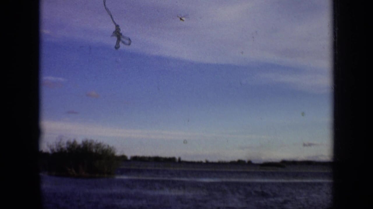 Lake and wooded shoreline seen under a blue sky with dark film-frame borders.