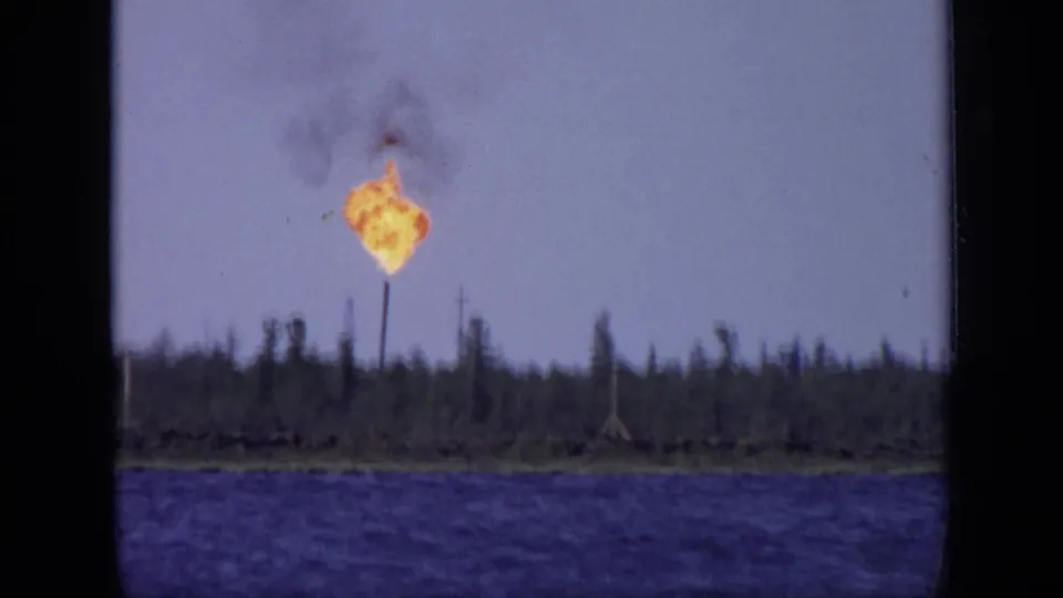A bright industrial flare and smoke plume rise beyond the lake in 1971 8mm footage attributed to the Moscow, Russia area.