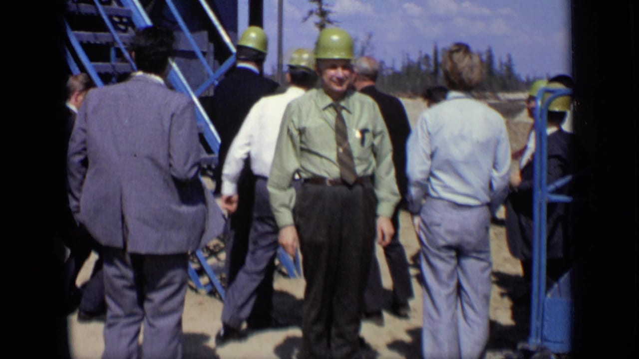 1971 Moscow frame of adult men in suits and green hard hats gathered near a blue metal staircase at a cleared industrial site.